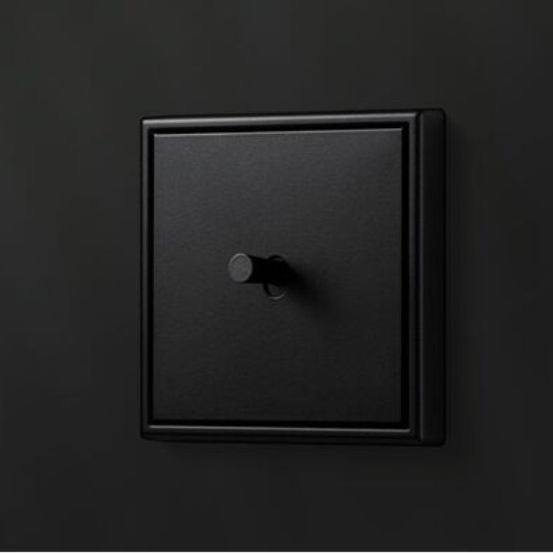 Schwarzer Kippschalter im modernen Design, quadratisch, an einer dunklen Wand montiert.