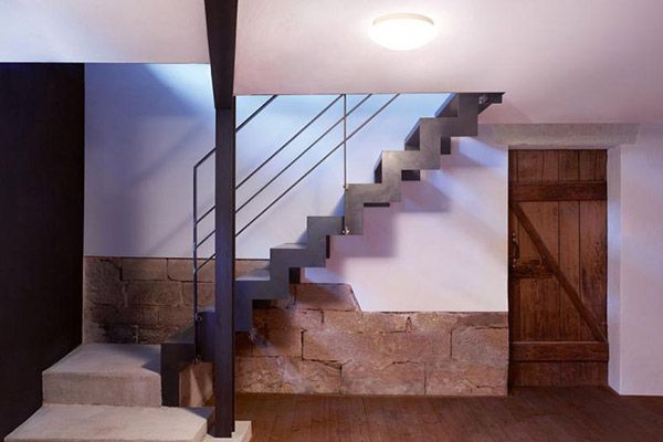 Bildquelle: Tylö Moderne Kellertreppe aus Metall mit Geländer, Steinwand, Holztür und Deckenleuchte, gut beleuchtet.